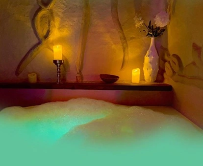 Bañera de hidromasaje con agua con luz verde y espuma y unas velas al fondo