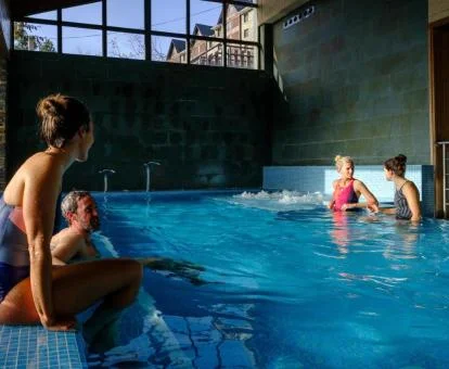 Personas disfrutando de la piscina cubierta con zona de relajación del spa.
