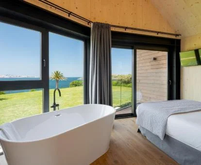 Habitación acogedora con bañera y amplios ventanales con vistas al mar de una de las cabañas del alojamiento.