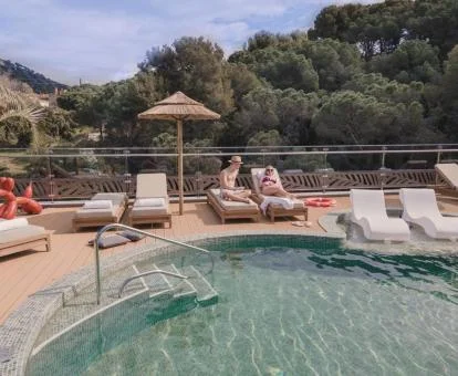 Piscina exterior del hotel con tumbonas sobre el agua, una pareja tomando el sol y vistas al bosque.