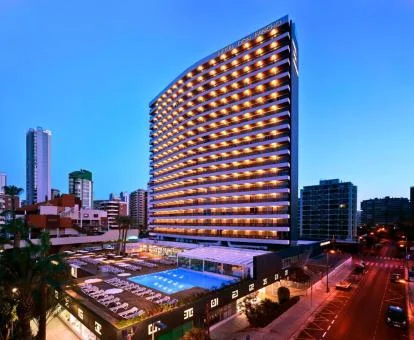 Precioso hotel de ciudad con iluminación nocturna y una gran piscina exterior.
