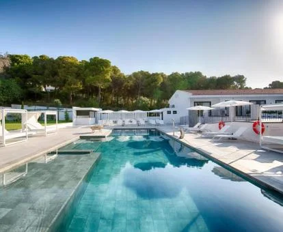 Amplia piscina exterior con camas en el agua y camas balinesas, rodeada de naturaleza.