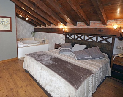 Foto de la Suite con bañera de hidromasaje junto a la cama que podemos ver al fondo de la foto y bajo unas vigas de madera que le da un toque con mucho encanto.