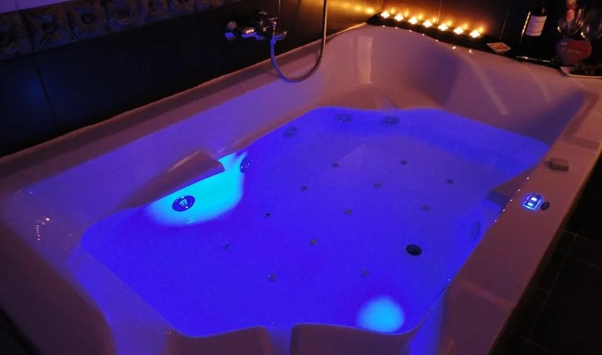 Foto de un jacuzzi con iluminación y unas velas en la parte del fondo en una habitación a oscuras donde resalta la luz del jacuzzi