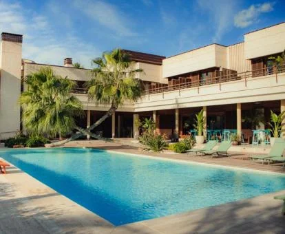 Precioso hotel con piscina exterior, tumbonas y palmeras, ideal para una escapada romántica en pareja.