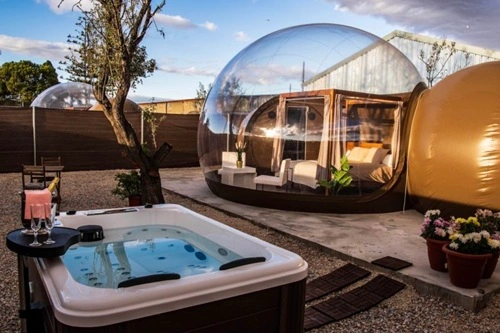 Foto de una burbuja transparente en medio del campo ideal para dos personas y con el jacuzzi en el exterior junto a la burbuja