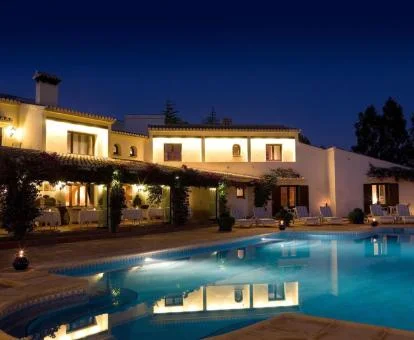 Hotel con encanto y piscina exterior con iluminación nocturna.