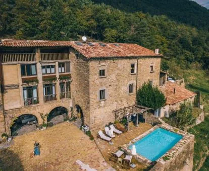 Edificio de piedra rodeado de vegetación con piscina y terraza solarium con vistas.