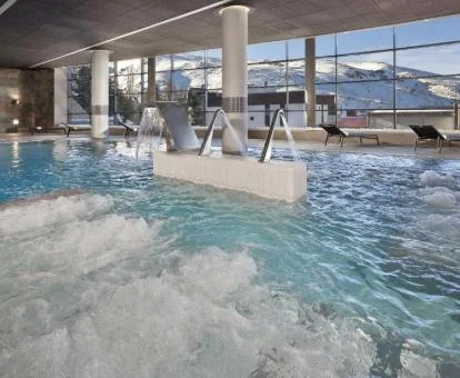 Espectacular piscina con elementos de hidroterapia del hotel y vistas a las montañas nevadas.
