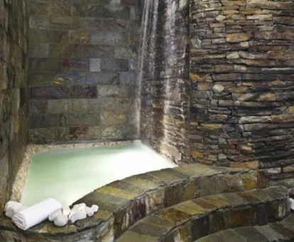 Acogedora piscina con cascada y paredes de piedra del centro de bienestar del hotel.
