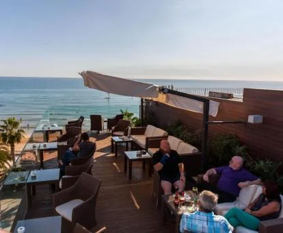 Varias personas disfrutan de la acogedora terraza con vistas al mar del hotel.