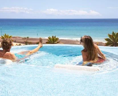 Pareja disfrutando de las camas de agua de la piscina con vistas al mar del hotel.