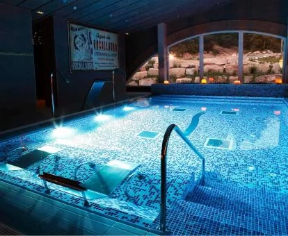 Amplia piscina con elementos de hidroterapia e iluminación nocturna del centro de bienestar del hotel.