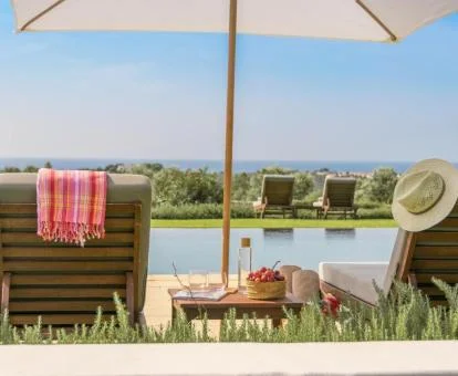 Piscina con vistas al mar y tumbonas rodeada de jardines.