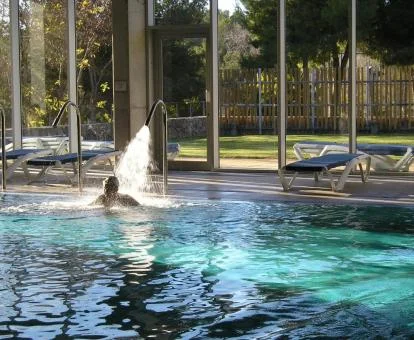 Persona disfrutando de la piscina cubierta con hidroterapia y vistas al exterior del centro de bienestar del hotel.